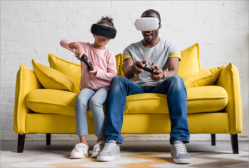 father and daughter in vr headsets playing video games on couch